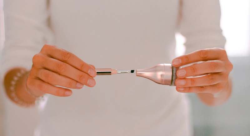 Woman using a handheld body contouring device on her abdomen in soft natural light